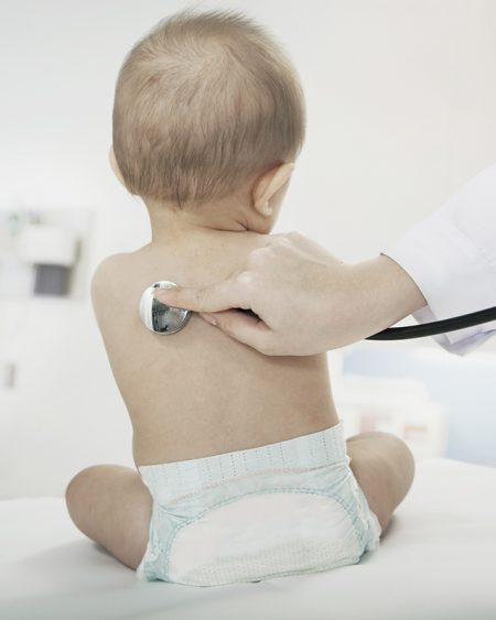 Baby sitting in the doctors office with the doctors hand checking heart beat with a stethoscope